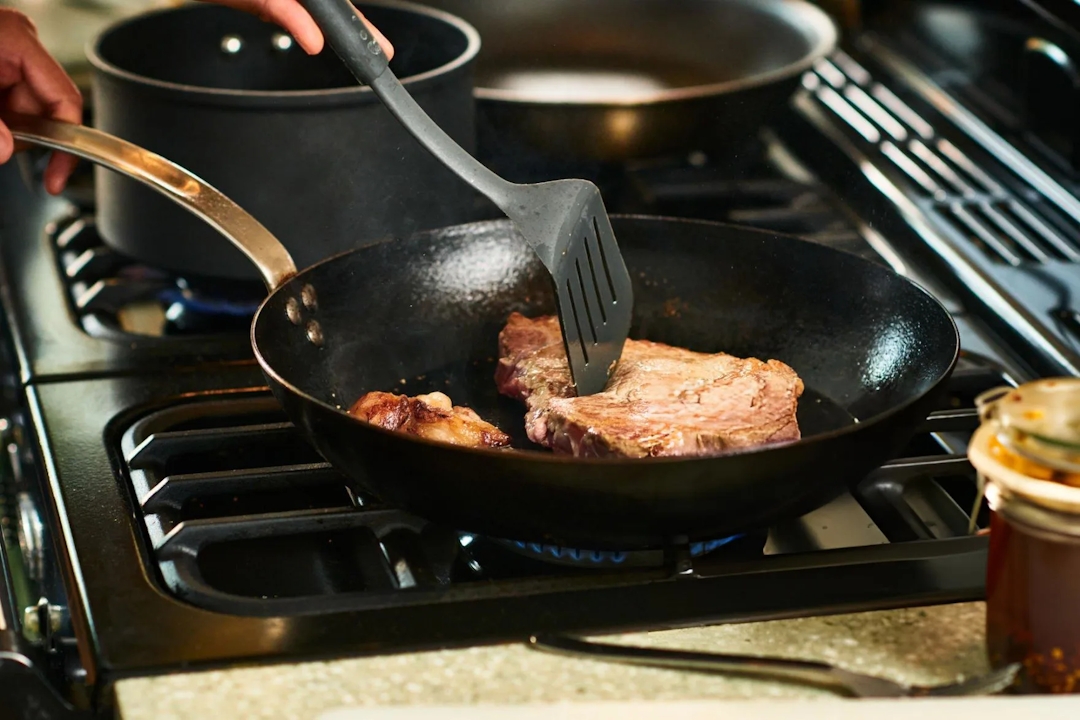 Person using spatula to cook steak in frying pan