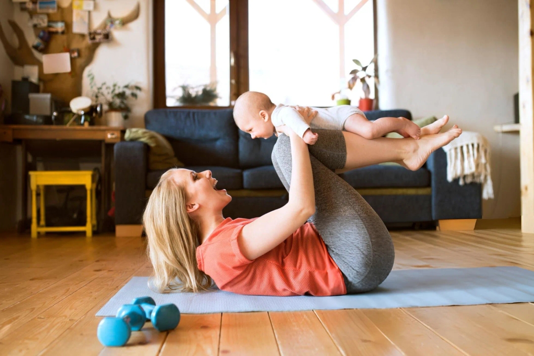 weight loss for busy mothers - Happy mother lifting up baby at home lying on mat