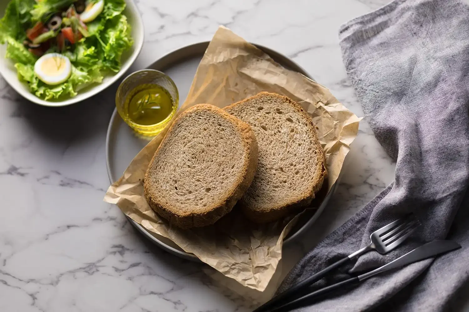 Choose This Bread for Weight Loss, Not Wheat two slices of bread sit on a plate next to a bowl of salad and a fork on a marble table
